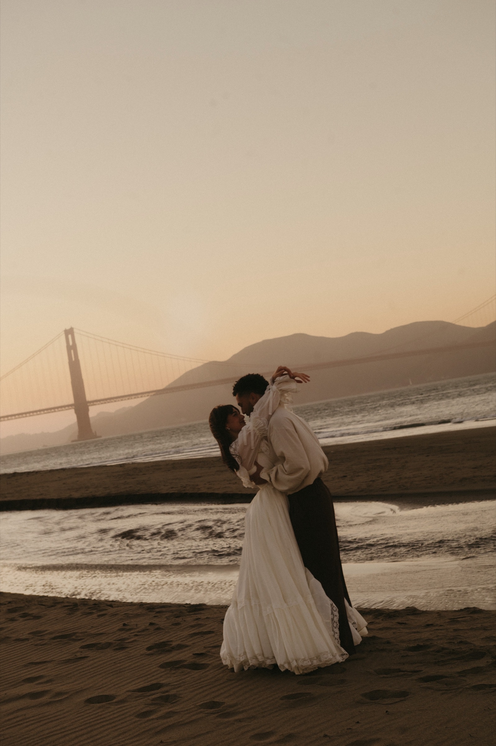 Berkeley and Robin dancing on the beach at sunset with the Golden Gate Bridge behind them